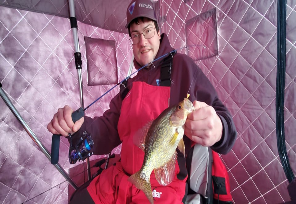 Capt. Johnathon Hosey holding a panfish inside an ice shelter