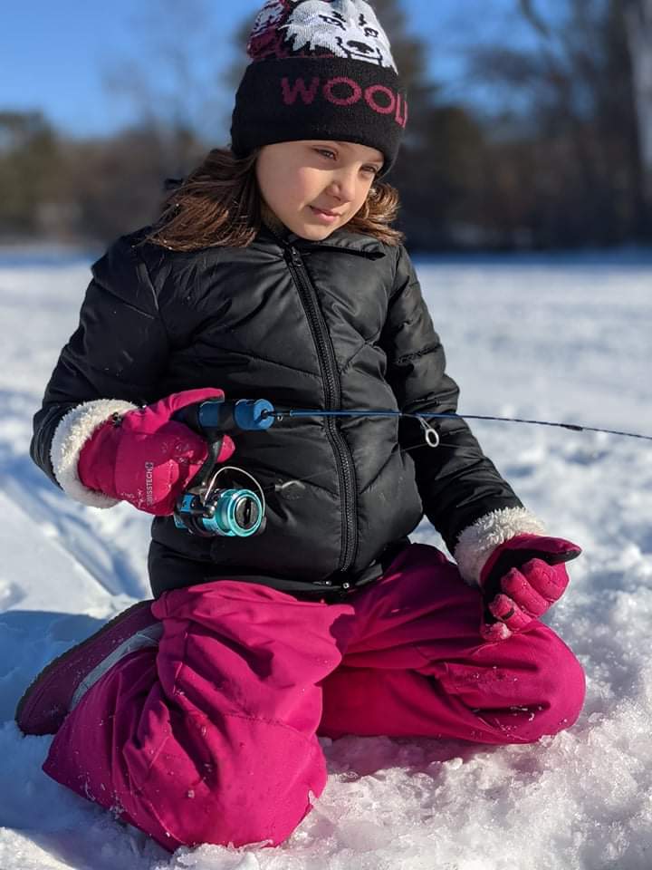 Lucia Stevens ice fishing with a small rod on a snowy lake