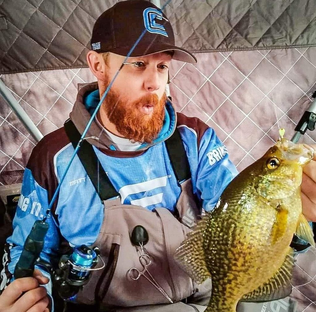 Matthew Stewart holding a sunfish inside an ice shelter
