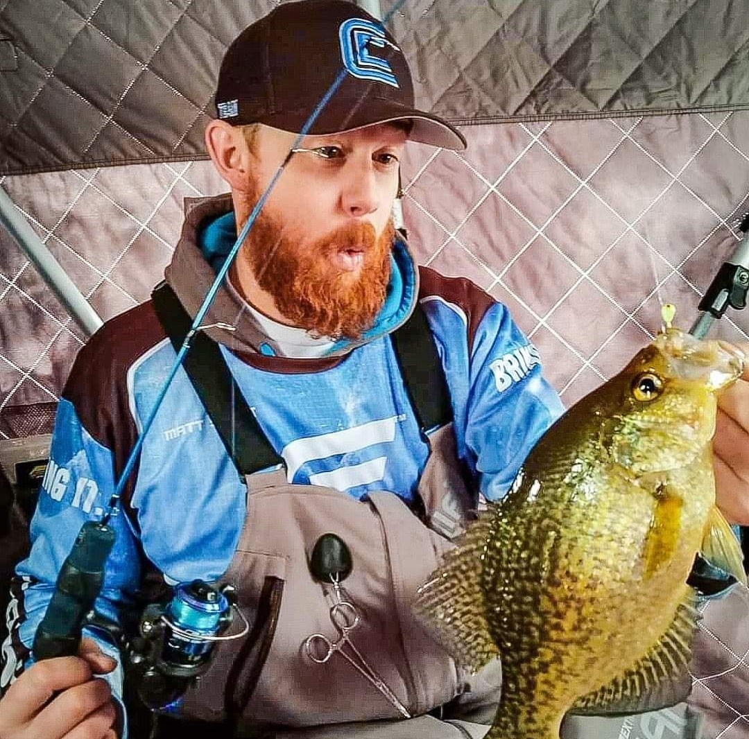 Matthew Stewart holding a sunfish inside an ice shelter