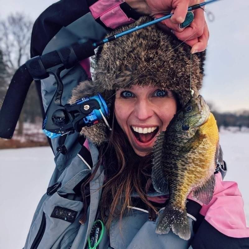 Stephanie Stevens holding an ice rod and a sunfish on a frozen lake